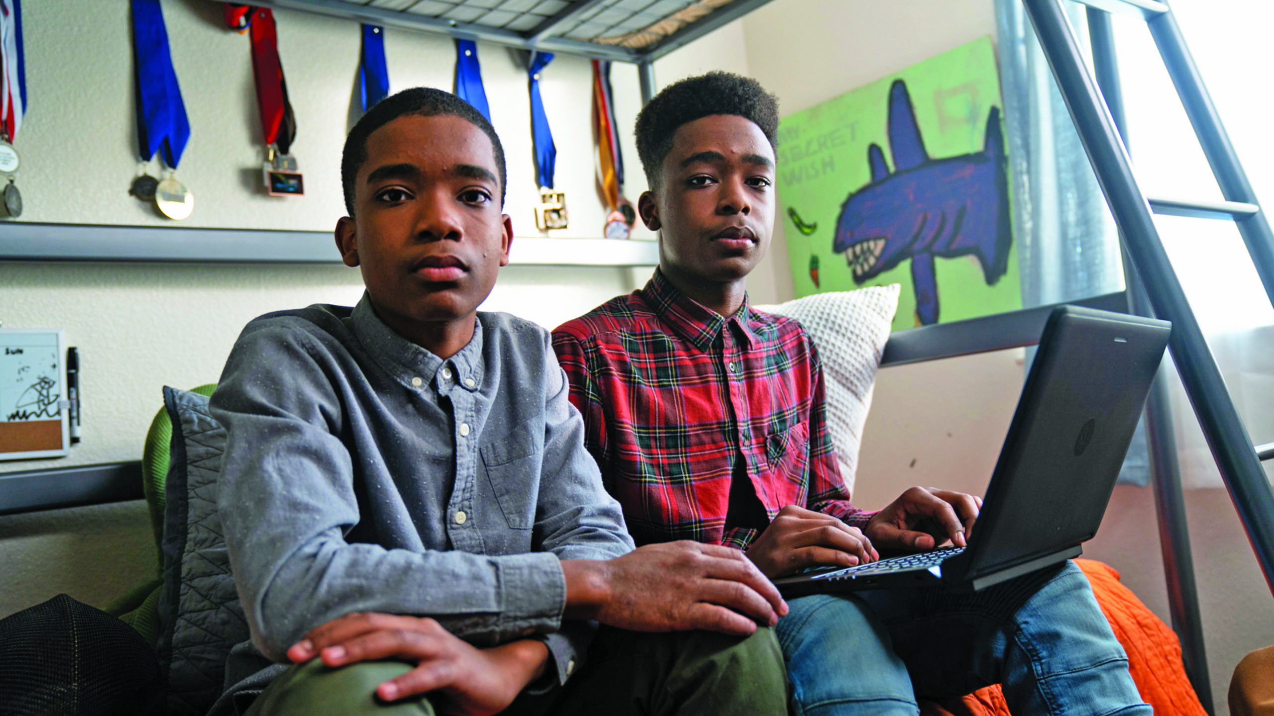 two high school-aged boys working on a laptop in a bedroom