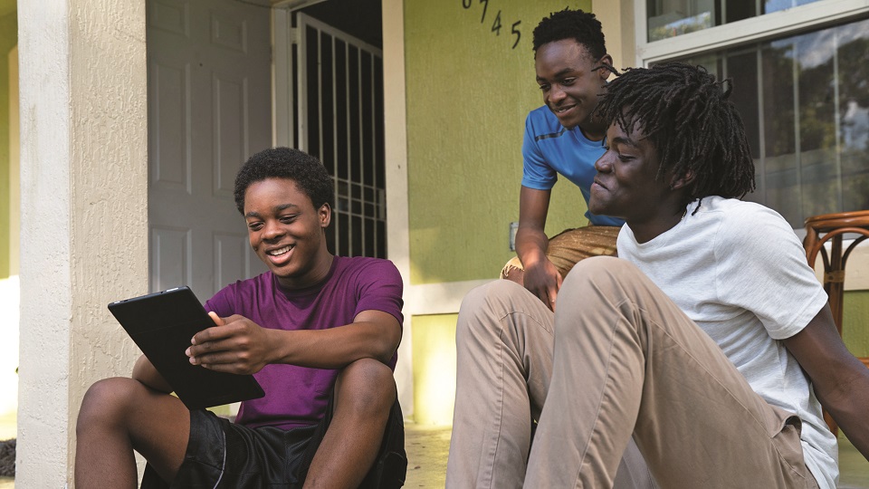 Three teen boys sitting on steps, looking at a tablet