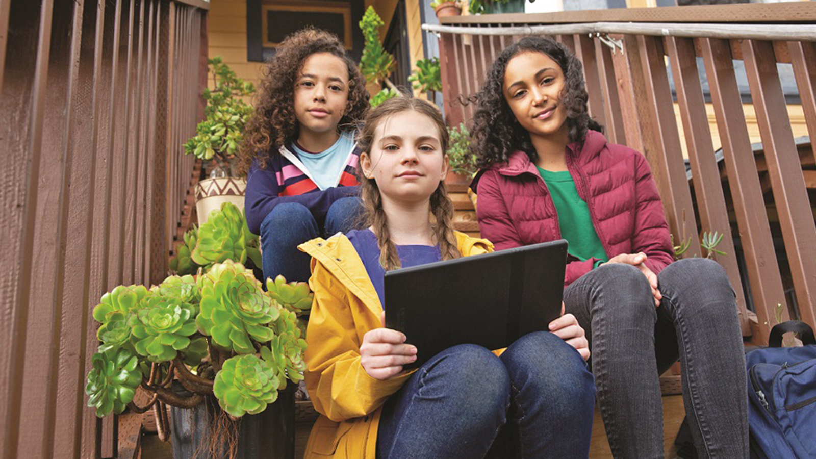 three girls sitting on steps looking at a laptop.