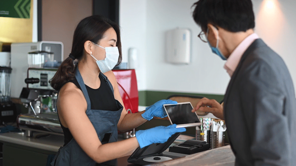 woman wearing mask, holding tablet for customer to use