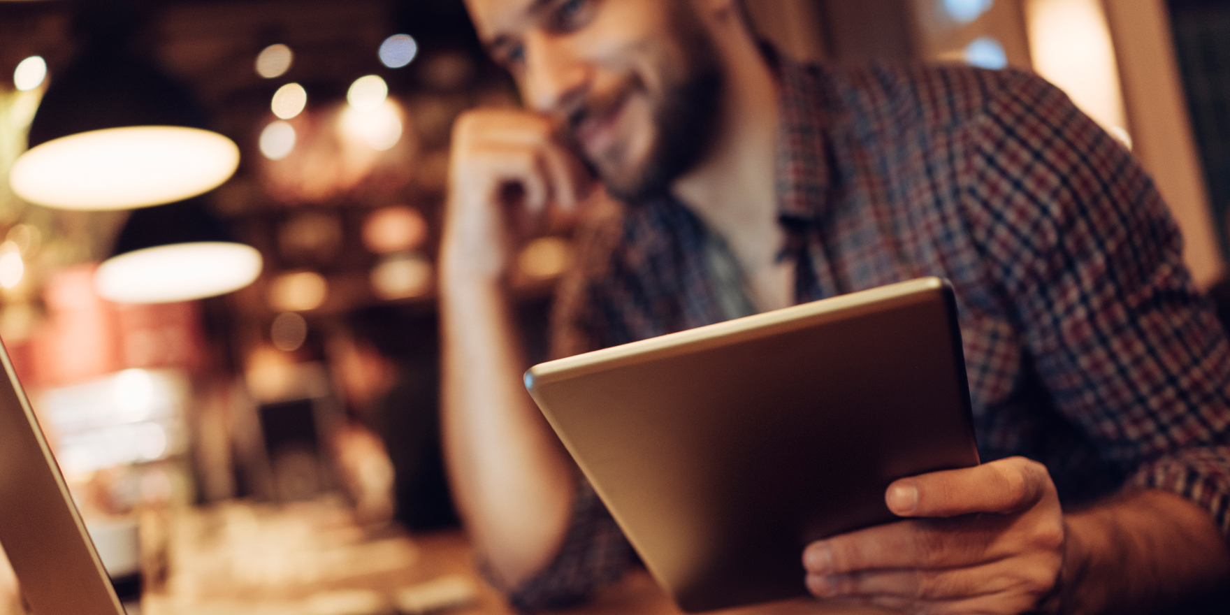 Man holding tablet, looking at laptop screen