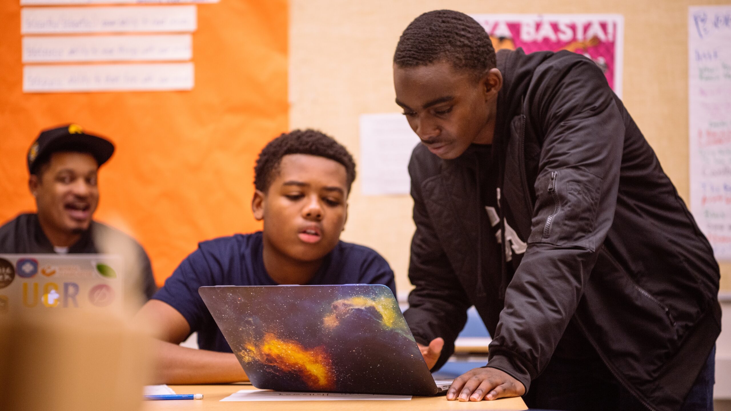 Man typing on a teen's laptop while the teenager looks on