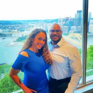 Photo of woman and man in front of window overlooking Pittsburgh