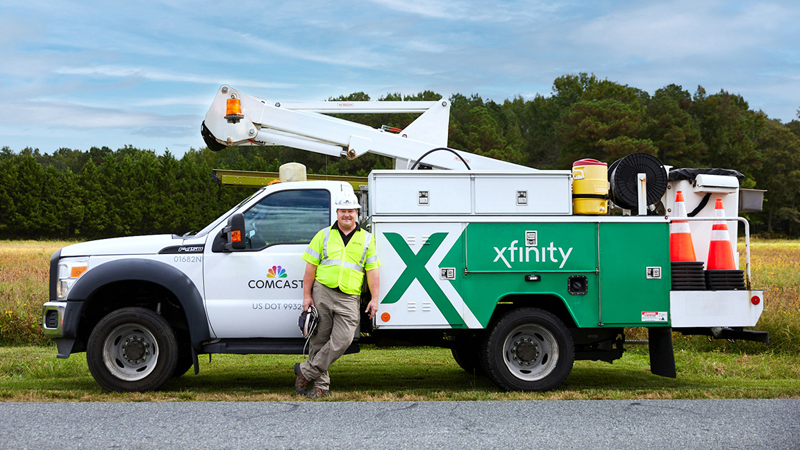 A technician standing in front of an Xfinity truck on a residential street.